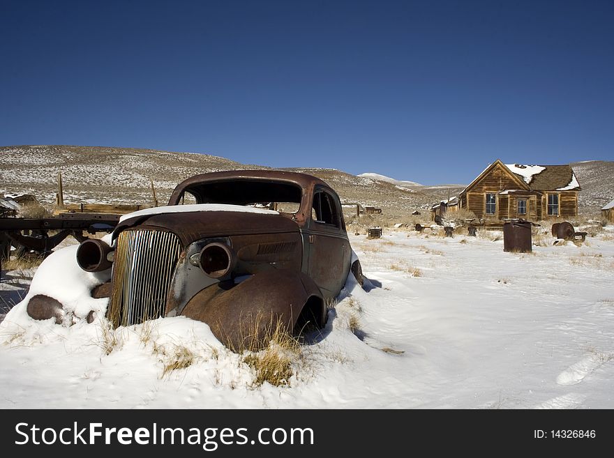 This is a old broken down rusted car sitting in the snow in a ghost town. This is a old broken down rusted car sitting in the snow in a ghost town.