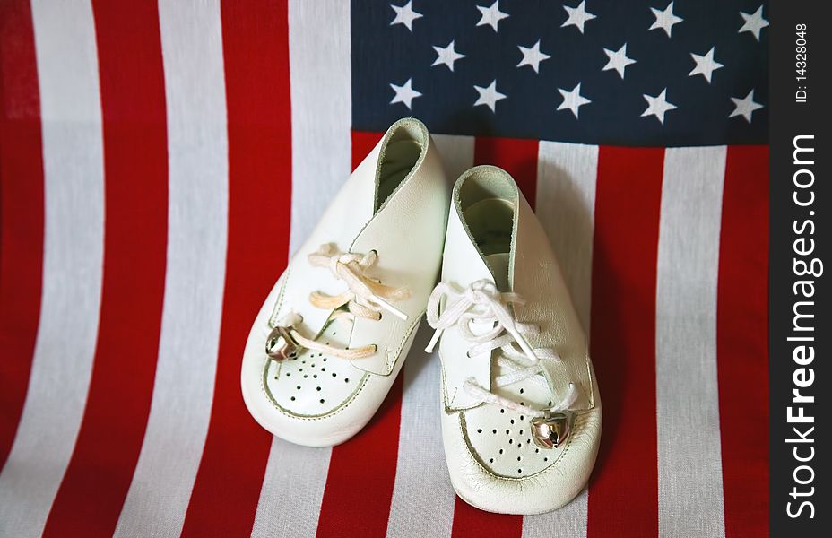 Pair of worn soft leather baby shoes, with bells attached to the laces, with an american flag background. Pair of worn soft leather baby shoes, with bells attached to the laces, with an american flag background.