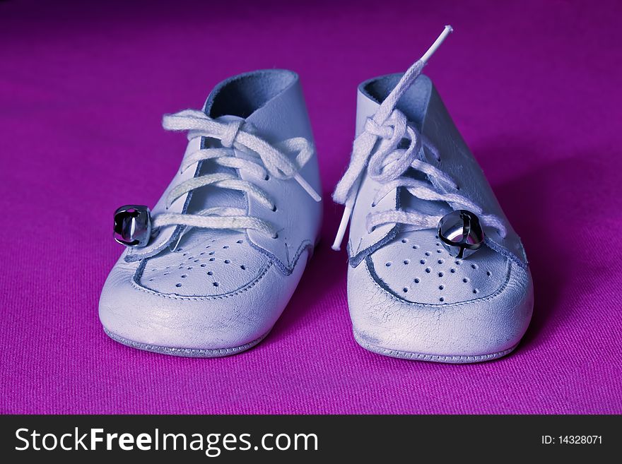 Soft white leather baby shoes with bells on the laces, on a pink/purple background. Soft white leather baby shoes with bells on the laces, on a pink/purple background