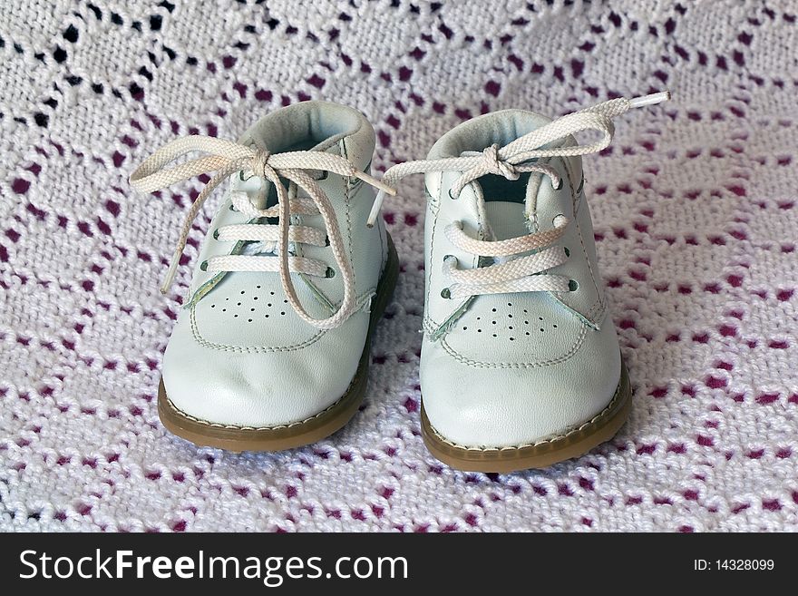 White leather baby shoes on a baby white crochet blanket background