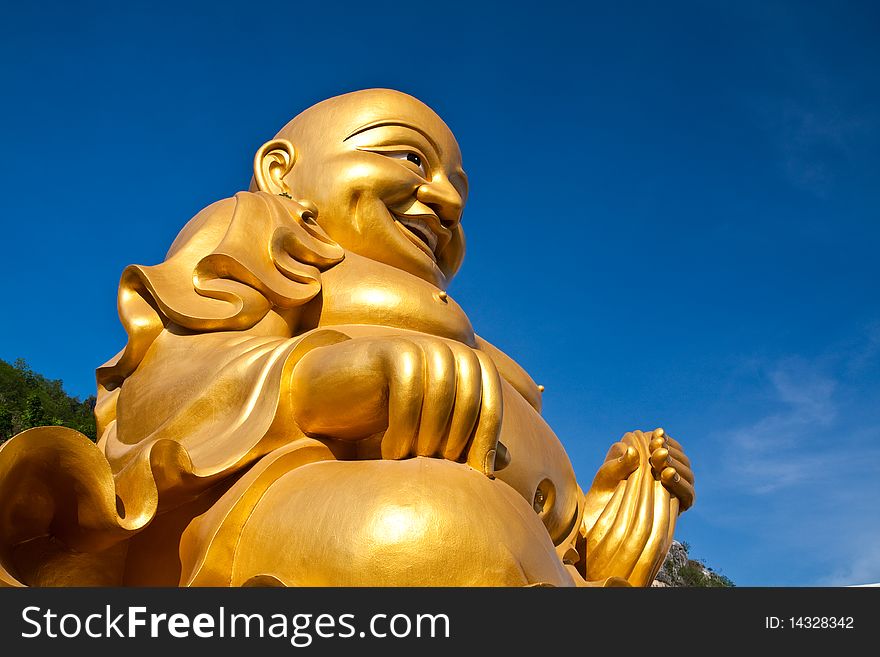 A big golden buddha disciple statue with the blue sky.