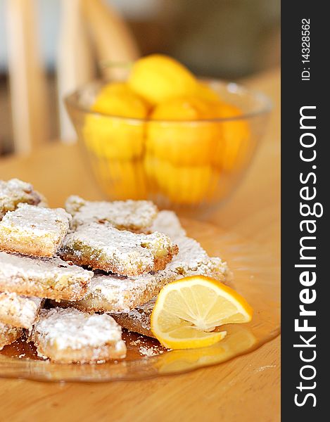 Plate of Powdered Sugar Dusted Lemon Shortbread Bars on Kitchen Table with Bowl of Lemons in Background