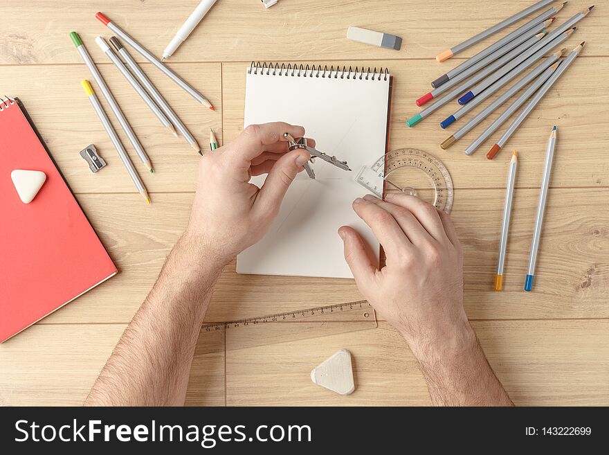 The designer draws a sketch in a notebook on a wooden table. Stationery. View from above