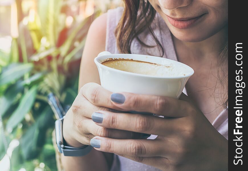 Close-up woman hands holding a white hot coffee cup and smelling coffee on green nature background