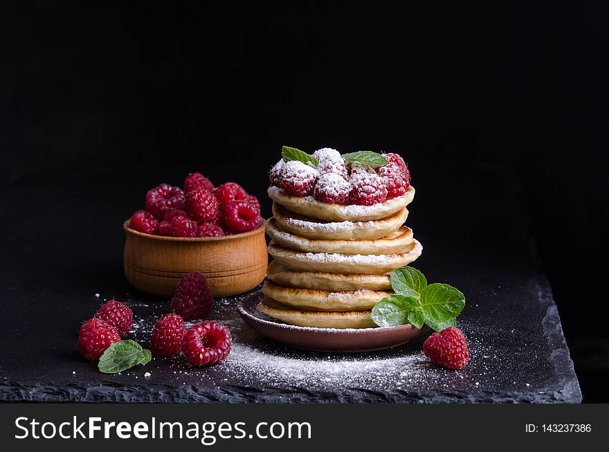 Pancakes with raspberries and berries around on black backgound