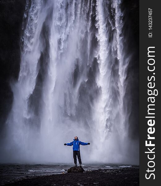 Male tourist in warm clothes stretching out arms and standing near Skogafoss Waterfall in Iceland. Male tourist in warm clothes stretching out arms and standing near Skogafoss Waterfall in Iceland