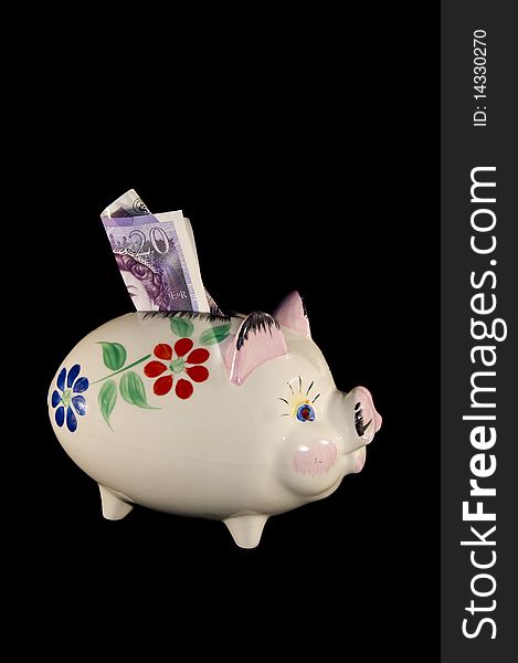 Old china piggy bank with flower pattern and money in the slot on a black background in portrait format. Old china piggy bank with flower pattern and money in the slot on a black background in portrait format