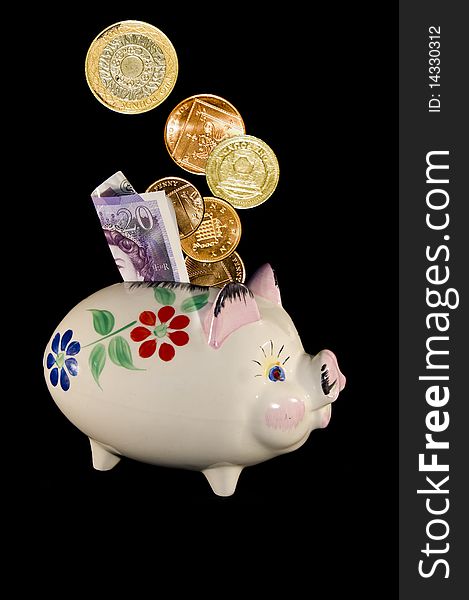 Old china piggy bank with flower pattern and money in the slot on a black background in portrait format. Old china piggy bank with flower pattern and money in the slot on a black background in portrait format