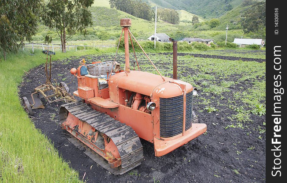 Tractor with springs exposed in the seat standing in a field with a tiller attached. Tractor with springs exposed in the seat standing in a field with a tiller attached