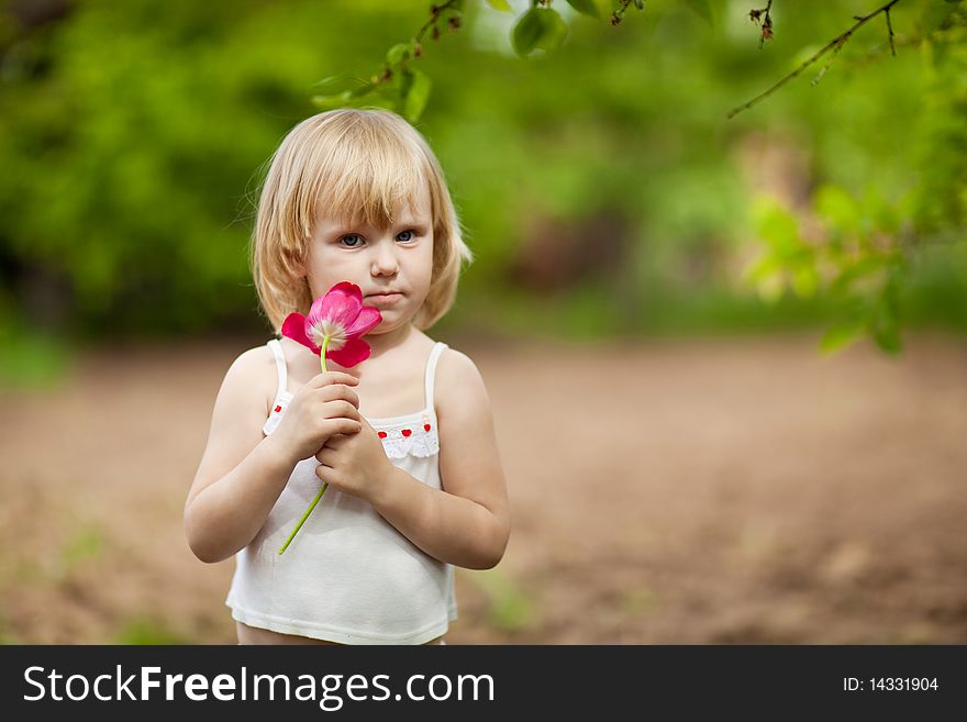 Small serious girl with tulip outdoors in sunny day