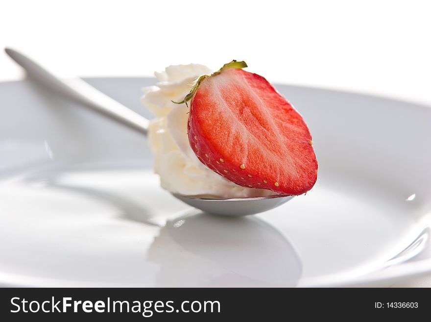 Single ripe fresh strawberry on spoon with cream isolated on white.