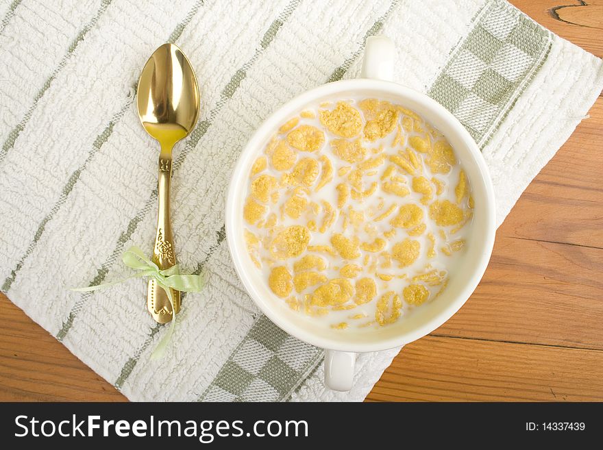On the wooden table is breakfast cereal with milk, spoon and napkin
