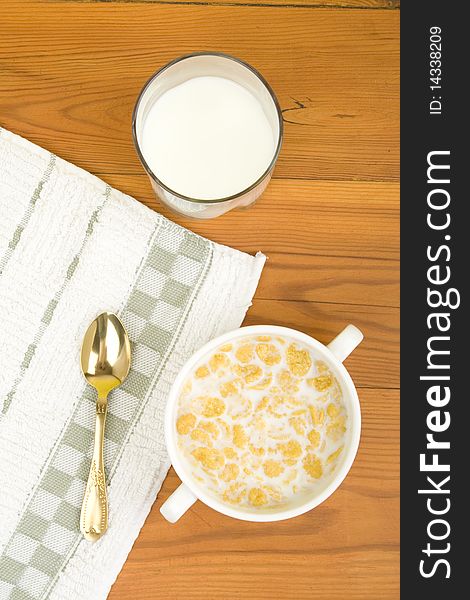 On the wooden table is breakfast cereal with milk, spoon and napkin