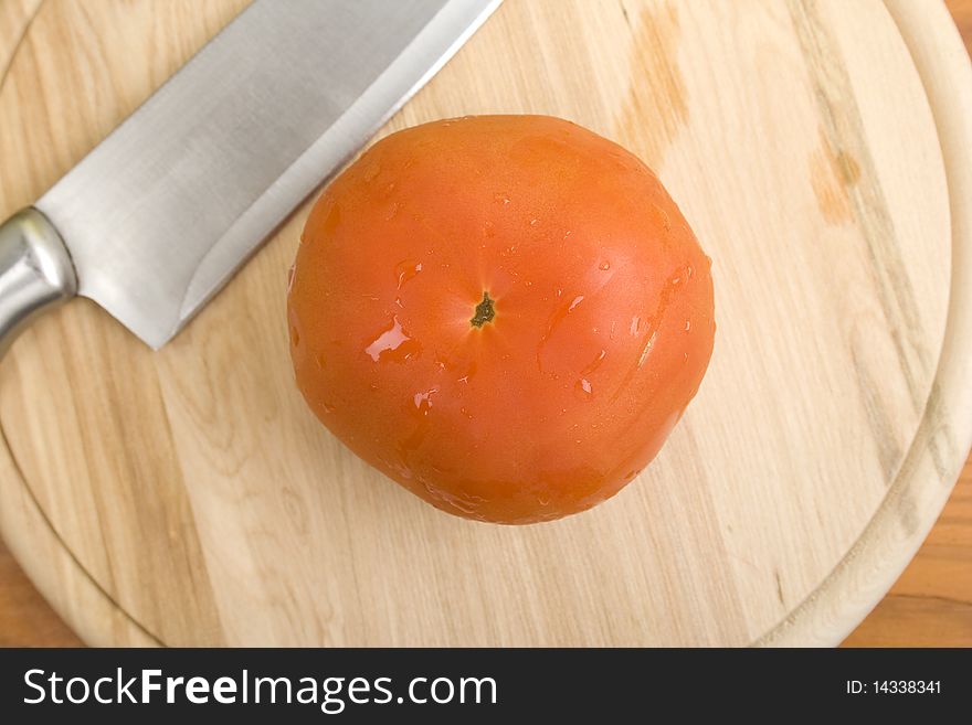 Red tomatoes on a wooden board near a knife