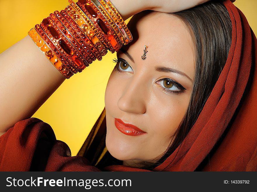 Young beautiful woman in indian traditional jewellery, bindi and make-up. yellow background