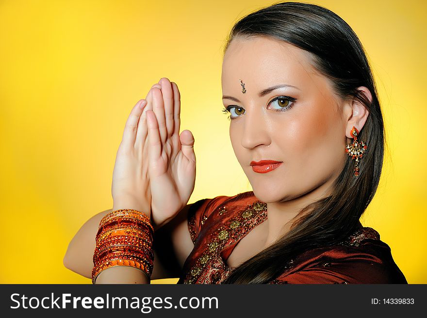 Young beautiful woman in indian traditional jewellery, bindi and make-up. yellow background. Young beautiful woman in indian traditional jewellery, bindi and make-up. yellow background