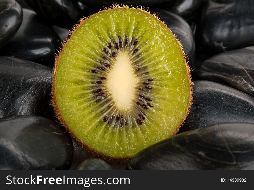 Half kiwi on dark stones close up