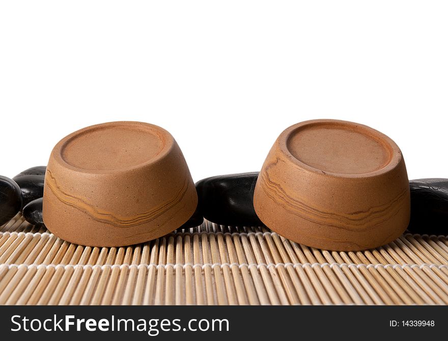 Two turned clay cups, mat and stones isolated in white