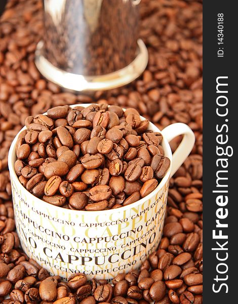 Fresh brown coffee beans in a cappuccino cup, metal coffee jar in the background