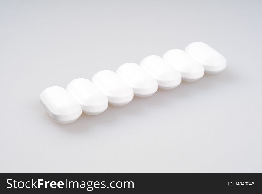 White pills packed in a row on a light background. Close-up.