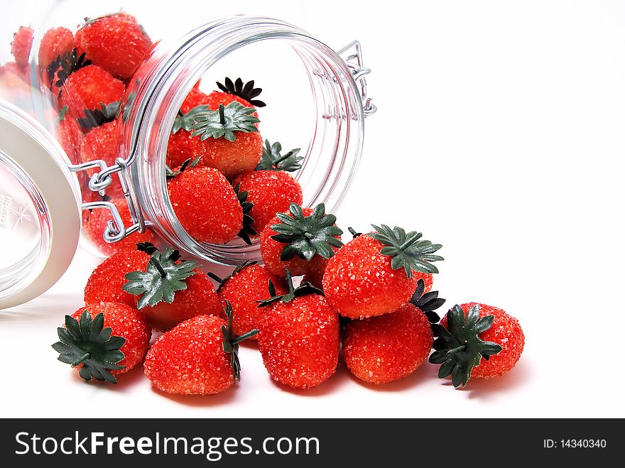 Spilled marzipan strawberries from the jar on the white background.
