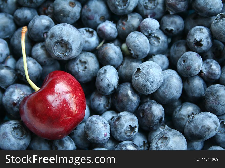 Cherry with stem sitting inside a bunch of blueberries. Cherry with stem sitting inside a bunch of blueberries