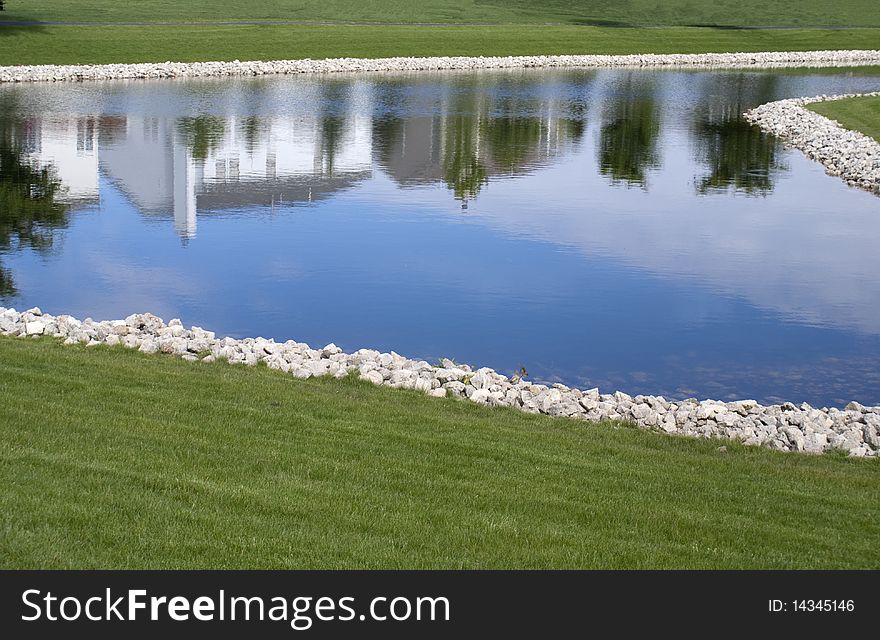 Suburban neighborhood reflected in bright blue waters of rock lined pond. Suburban neighborhood reflected in bright blue waters of rock lined pond.