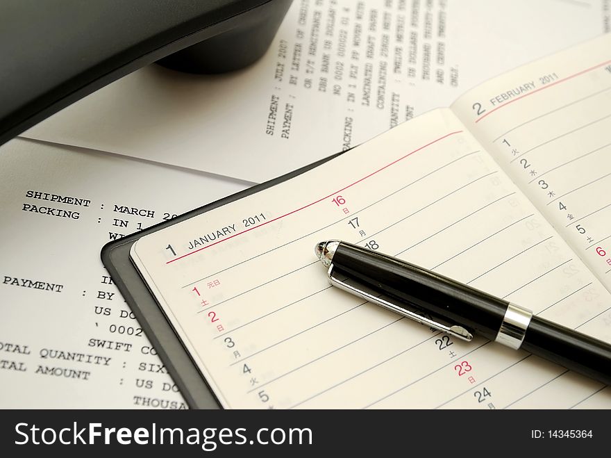 Capped black pen on planner with phone signifying concepts such as office and business, planning for the new year, financial budget and work related objects. Capped black pen on planner with phone signifying concepts such as office and business, planning for the new year, financial budget and work related objects