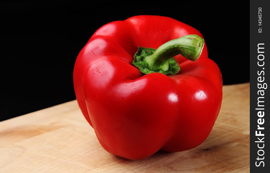 Fresh red bell pepper, sitting on a wooden cutting board, against a dark background. Fresh red bell pepper, sitting on a wooden cutting board, against a dark background.