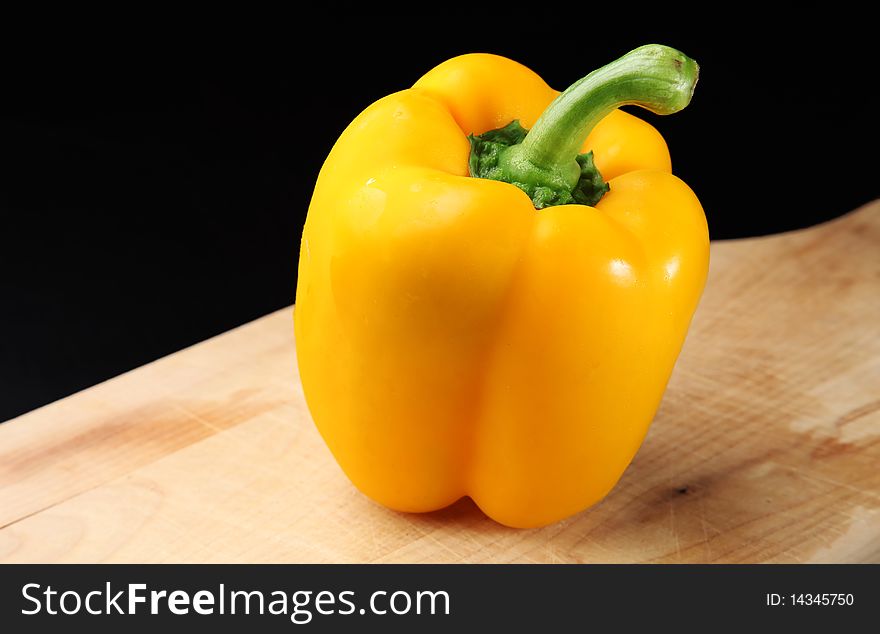 Fresh yellow bell pepper, sitting on a wooden cutting board, against a dark background. Fresh yellow bell pepper, sitting on a wooden cutting board, against a dark background.