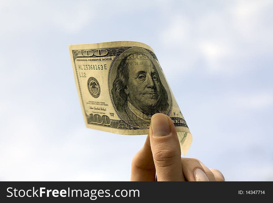 Hundred dollars in a female hand on a background of the light-blue sky. Hundred dollars in a female hand on a background of the light-blue sky