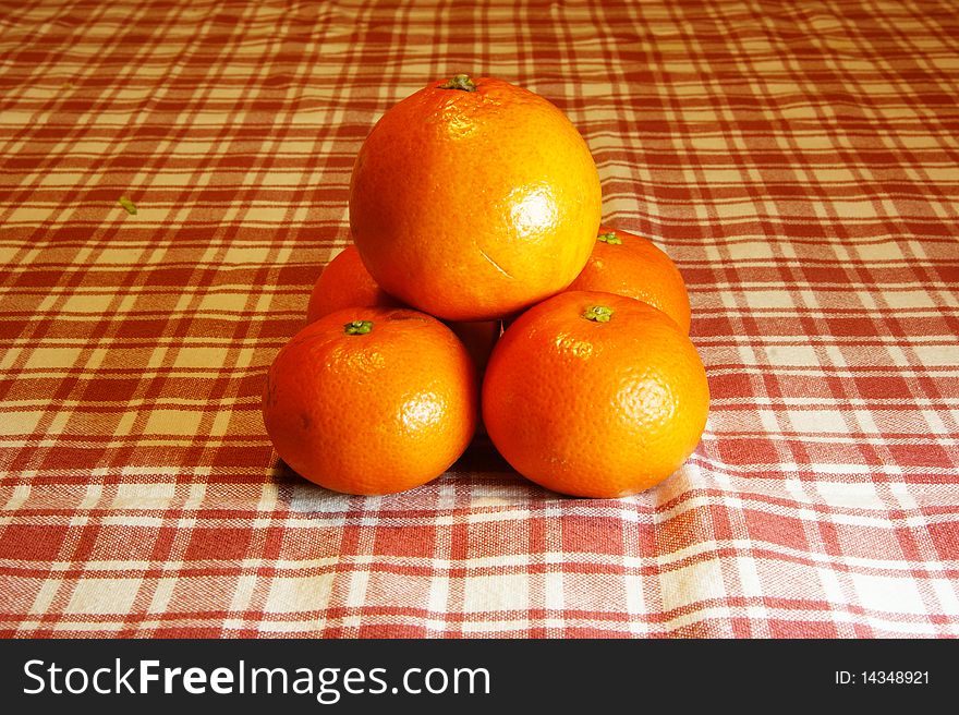 Pyramid of oranges and mandarins into a background with plaid tablecloth.