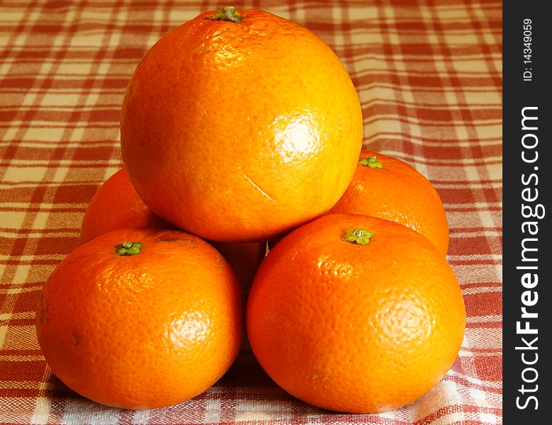 Pyramid of oranges and mandarins into a background with plaid tablecloth.