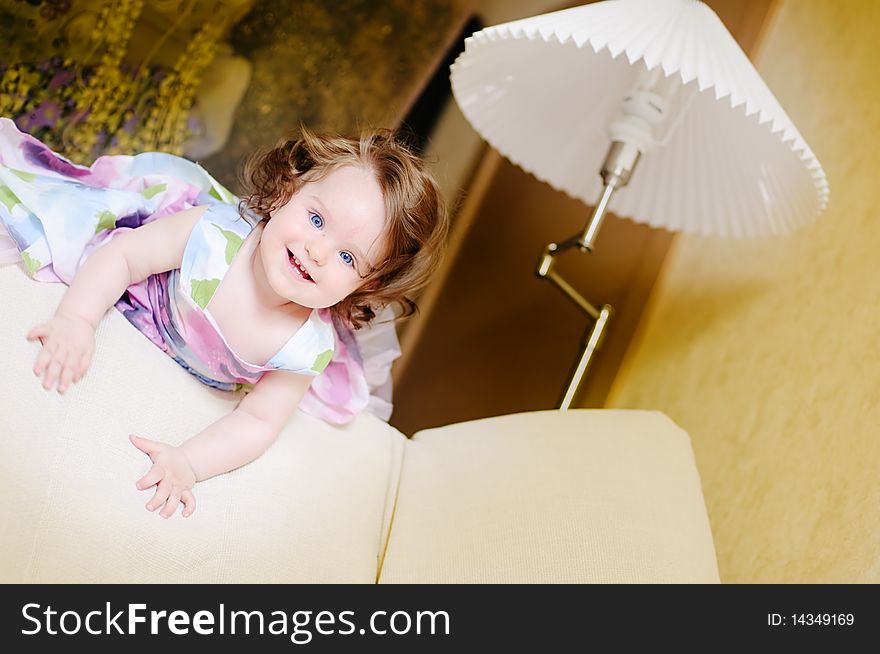 Baby-girl well-dressed lies on sofa near lampshade and smile. Baby-girl well-dressed lies on sofa near lampshade and smile