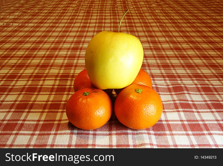 Pyramid of oranges and apple into a background with plaid tablecloth.