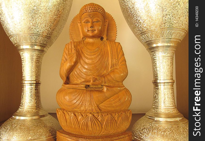 Wooden sculpture of gautam buddha in between silver stands.