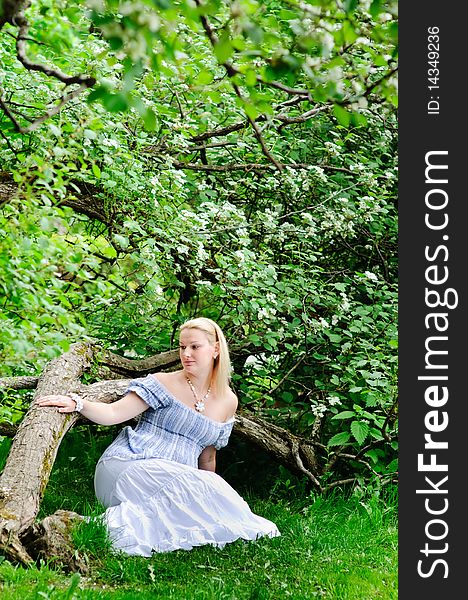 Beautiful pregnancy woman sits on the grass under the big blooming tree. Beautiful pregnancy woman sits on the grass under the big blooming tree