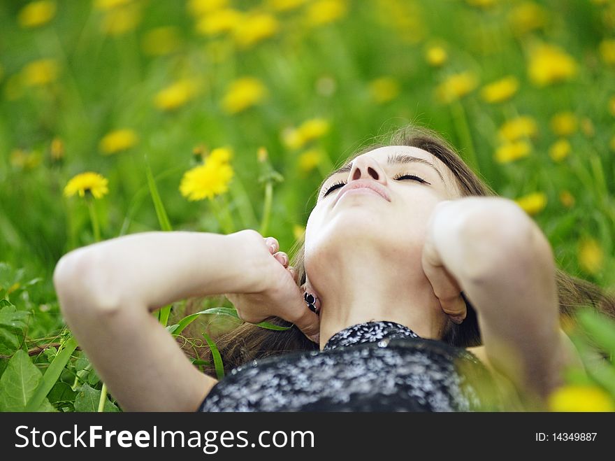 The girl lying in a green grass with yellow wild flowers