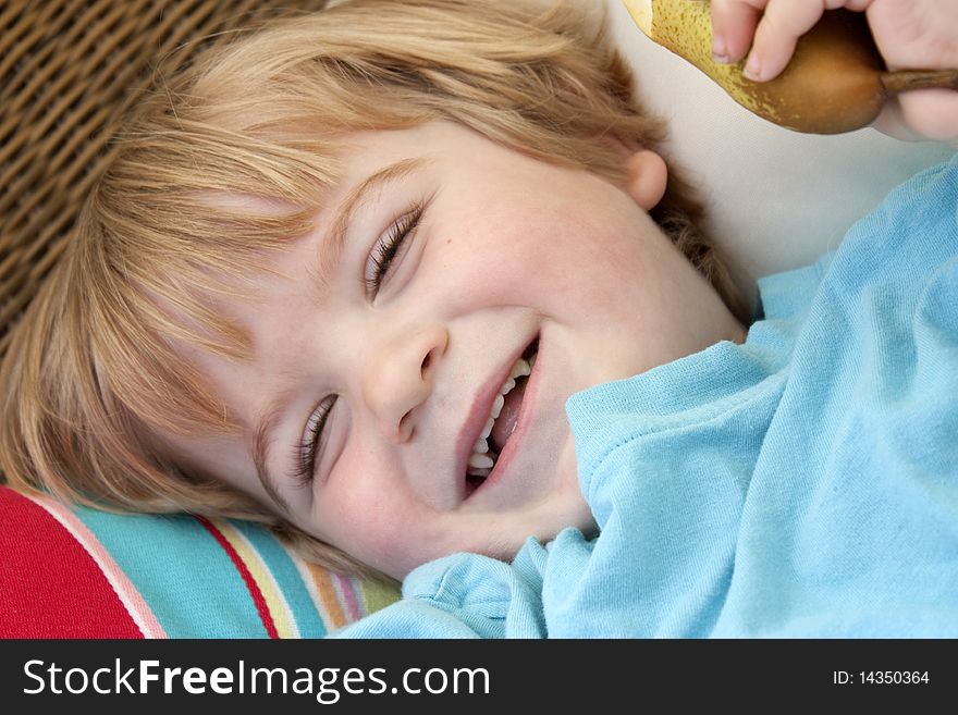Little boy holding a pear laying on some cushions laughing