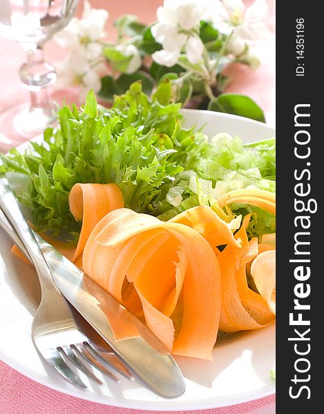 Salad from fresh vegetables for dinner. On a background a glass with water. A photo on a pink background