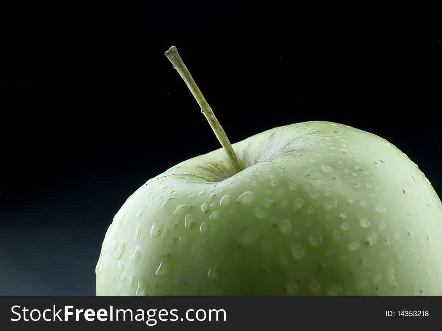 Image of a fresh green apple on a few drops of water behind a pleasant light on a black background