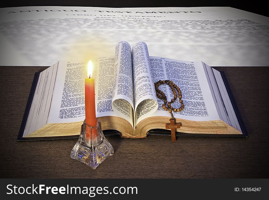 The Holy Bible, a rosary and a candle, on a background of a page of the Bible