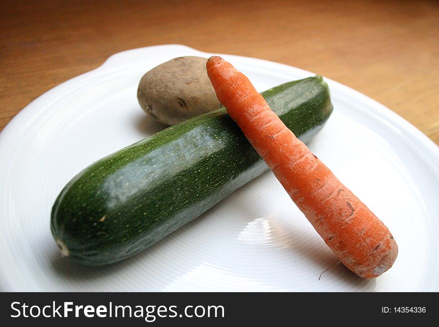 A carrot, cucumber, potato on a white dish. A carrot, cucumber, potato on a white dish
