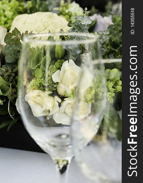 Wineglass and roses on a table set, focus on white rose behind the glass