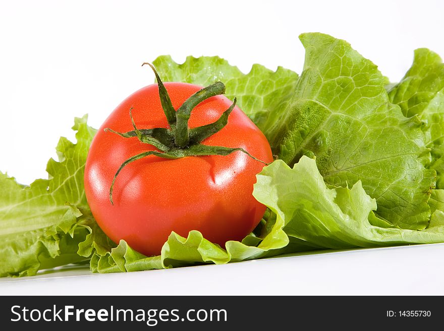 Red tomato in green leaves of salad. Red tomato in green leaves of salad