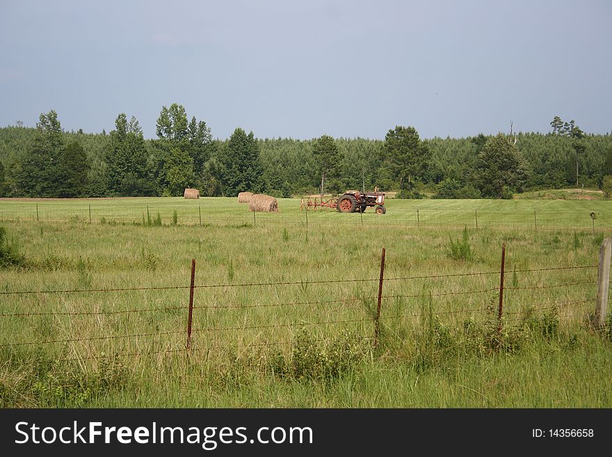 An old red tractor and a hay bale in a rural Alabama field. An old red tractor and a hay bale in a rural Alabama field.
