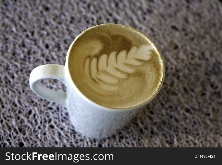 Cappuccino in a white mug on a dark white texture with a fern leaf motif in foam. Cappuccino in a white mug on a dark white texture with a fern leaf motif in foam