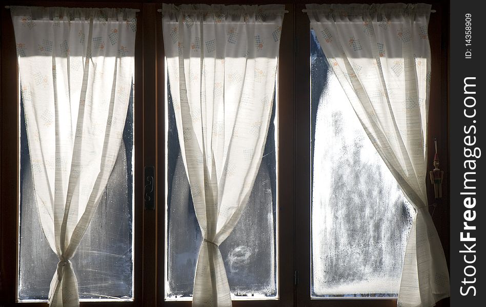 A window with curtains and cloudy glasses, in winter