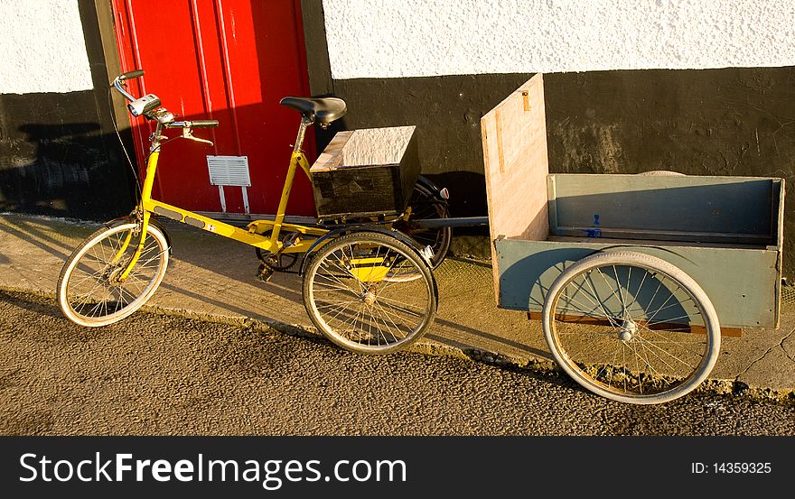An image of a tricycle with trailer parked beside a red hotel door. An image of a tricycle with trailer parked beside a red hotel door.