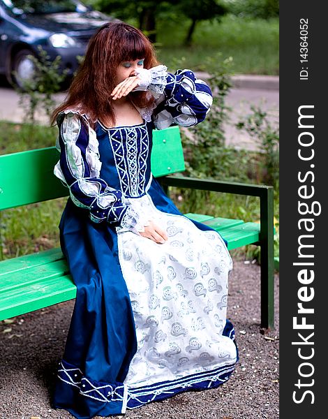 A girl in medieval blue dress sitting on a bench. A girl in medieval blue dress sitting on a bench